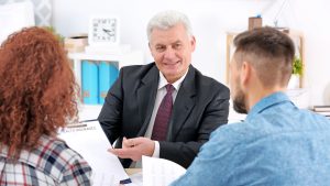 Three people sitting at an office desk reviewing paperwork for Life insurance. The Independent Insurance Agent is taking the time to explain all the details of the policy to his new clients