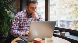 A Business Owner sitting in a coffe shop scrolling through documents on his laptop thinking about purchasing General Liability insurenance for his Woodstock, GA through White Oak Insurance Services.